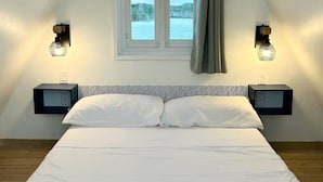 A bedroom with a bed, two bedside tables, a window with curtains, and a picture on the wall.