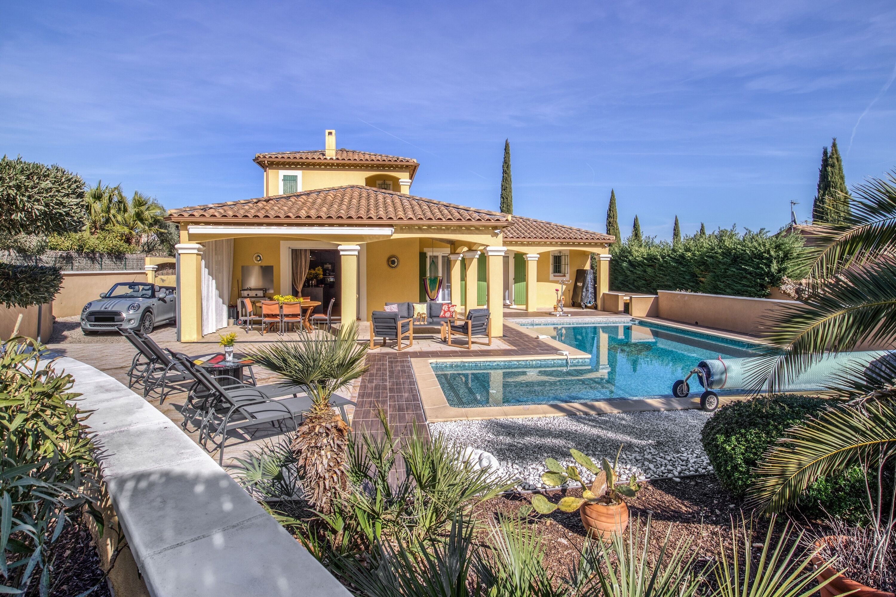 A yellow villa with a swimming pool, outdoor seating, and a car parked outside.