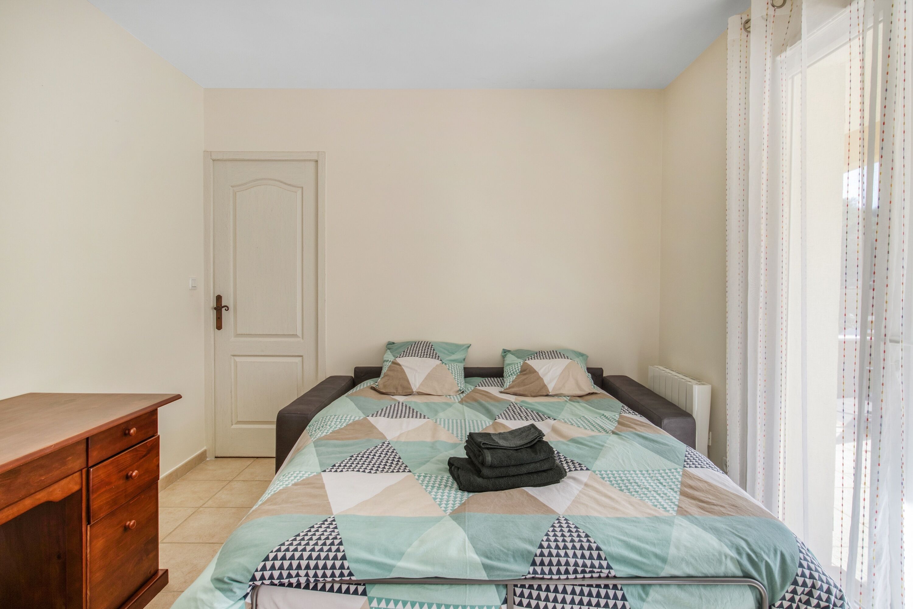 A bedroom with a bed, a wooden dresser, and a door.