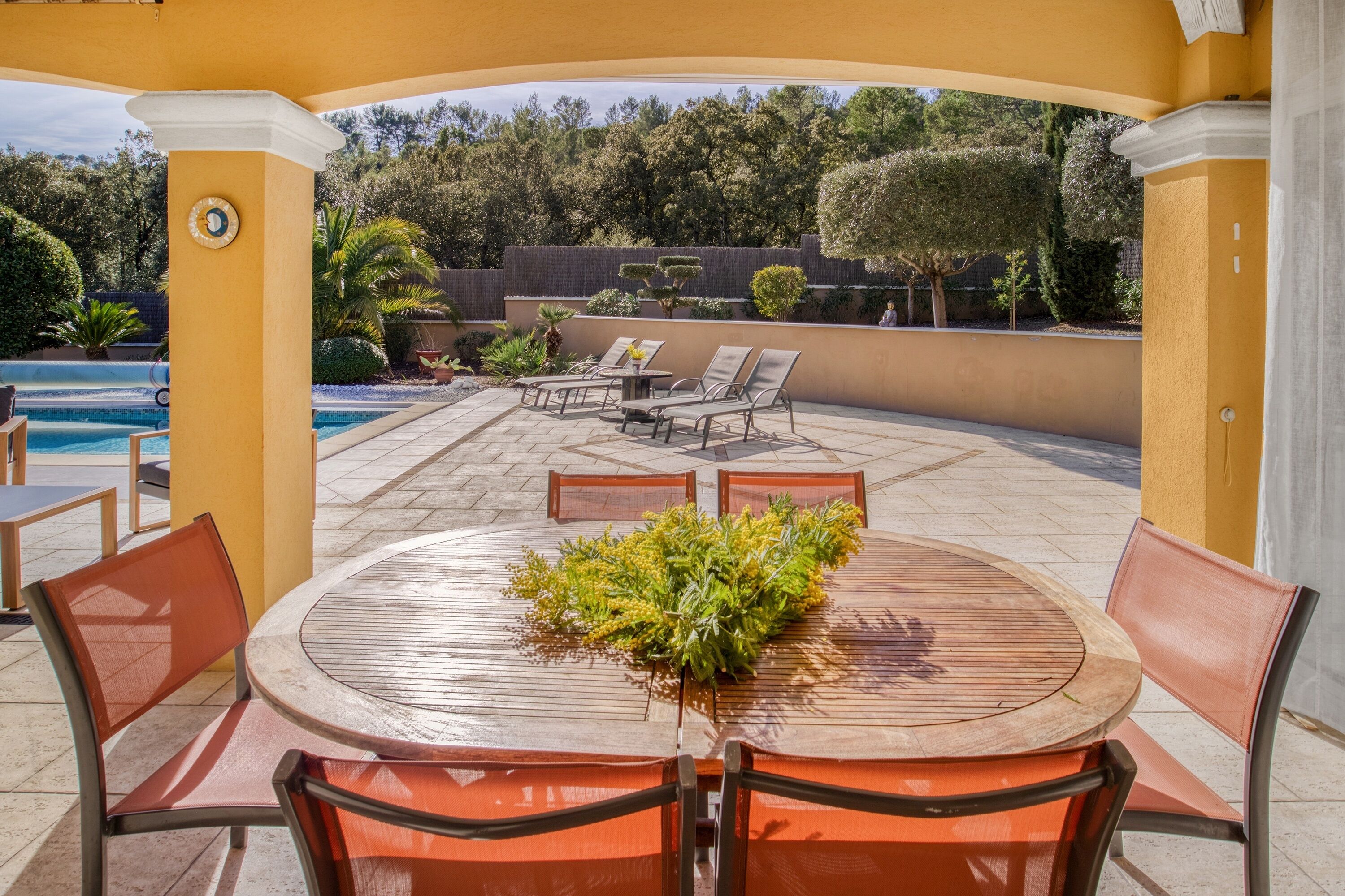 An outdoor patio with a round wooden table, orange chairs, and a decorative plant centerpiece.