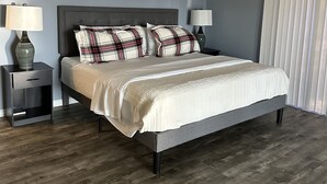 A bedroom with a bed, two nightstands, and a window with blinds.