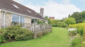 A stone house with a sloped roof, a wooden deck, and a well-maintained garden. - Glyde House (Dorchester)