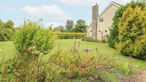 A house with a stone chimney, surrounded by a well-maintained garden with various plants and flowers. - Glyde House (Dorchester)