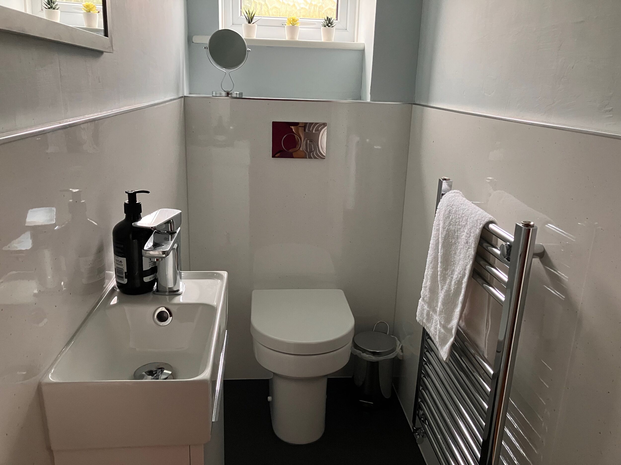 Ein kleines Badezimmer mit einem weißen Waschbecken, einer Toilette, einer kleinen Mülltonne und einem Handtuchhalter.