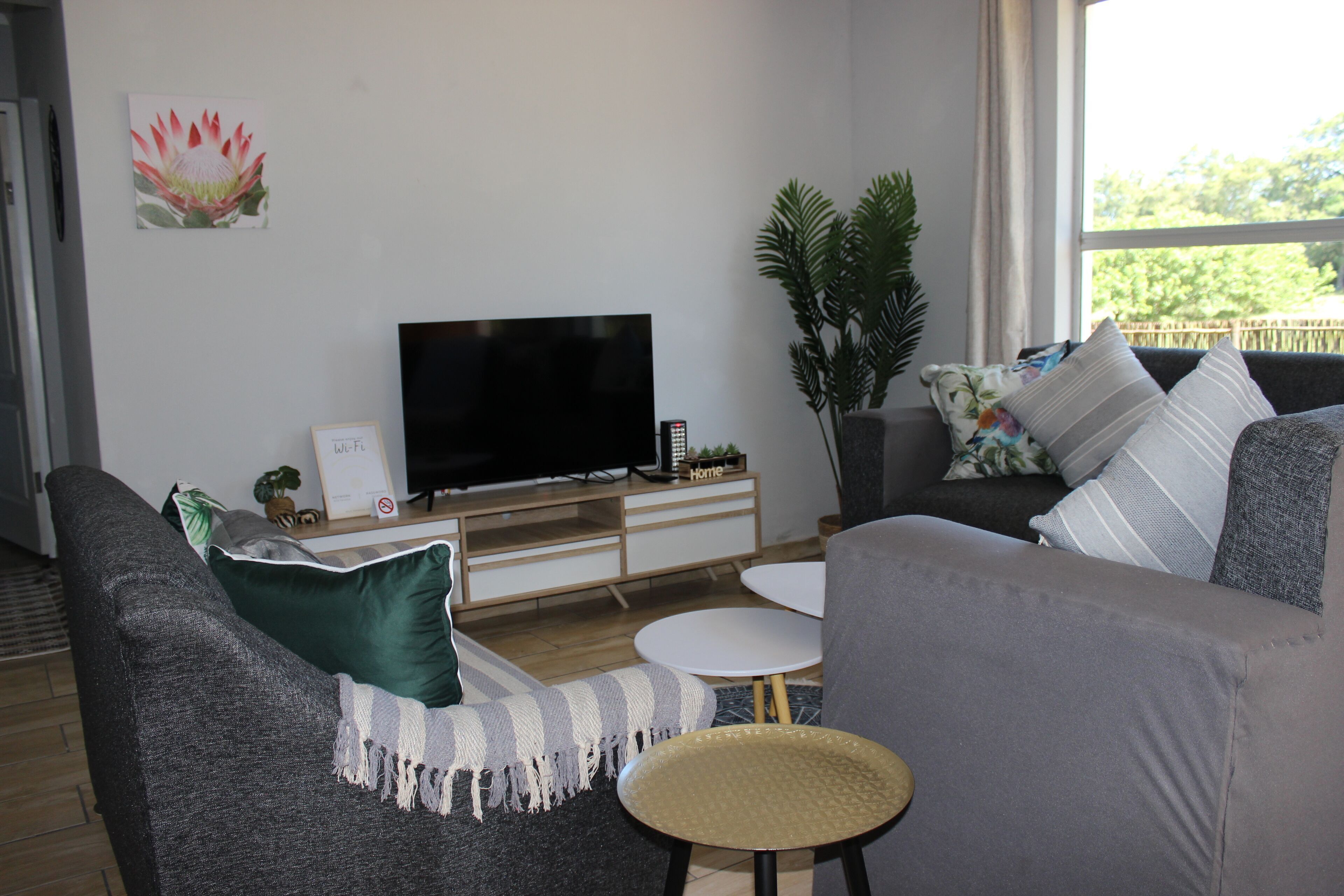 Uma sala de estar moderna com uma televisão de tela plana, sofás cinzas, uma mesa redonda pequena e um vaso com planta.