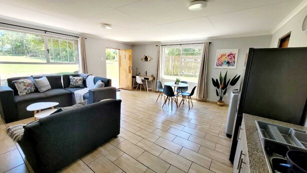 Una sala moderna con un sofá, una mesa de comedor con sillas y una cocina con refrigerador.