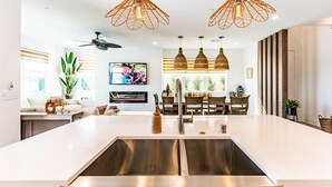Une cuisine moderne dotée d’un grand îlot central, d’appareils électroménagers en acier inoxydable et de luminaires suspendus.