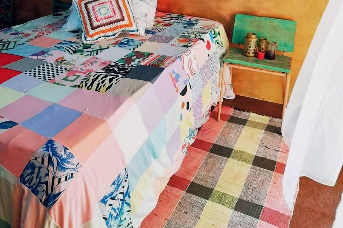 A room with a bed covered in a colorful quilt, a woven headboard, and a decorative paper flower arrangement above the bed.
