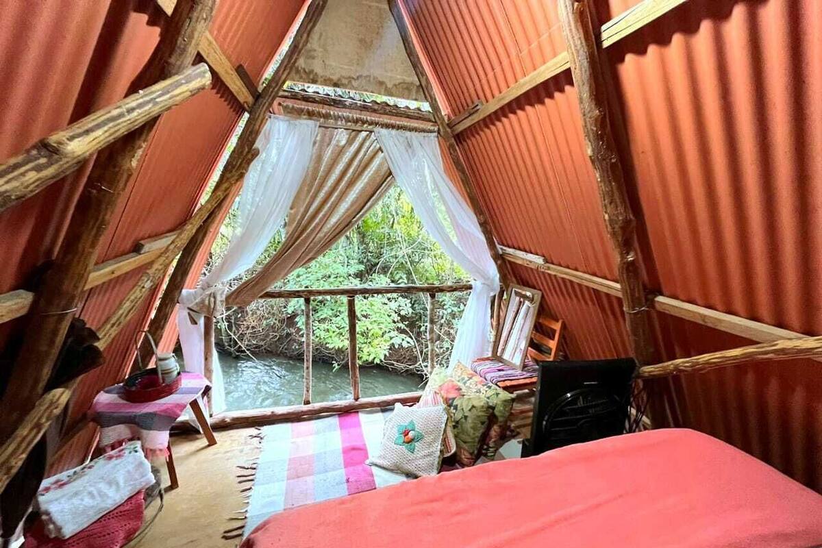 A cozy, triangular-roofed room with a bed, a small table, and a chair.