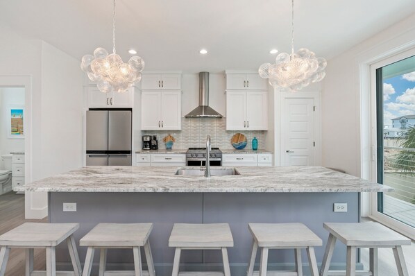 A modern kitchen with a large island, white cabinetry, stainless steel appliances, and pendant lighting.