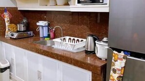Una cocina con armarios blancos, microondas, hervidor y refrigerador.