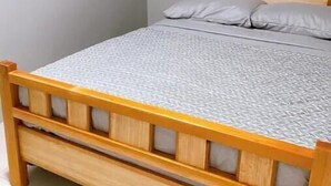 Una cama individual con estructura de madera y colcha gris estampada.