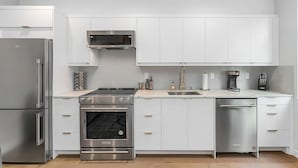 A modern kitchen with white cabinets, stainless steel appliances, a built-in oven, and a dishwasher. - Time Travelers Cowboys Sweet Suite (Seattle)