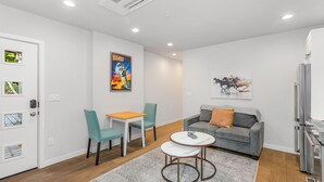 A modern living room with a grey sofa, teal chairs, a small white table, and a grey rug. - Time Travelers Cowboys Sweet Suite (Seattle)