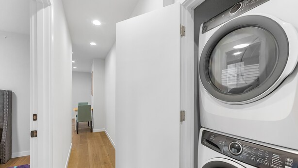 A laundry room with a washing machine and dryer, a door leading to a hallway, and a patterned rug on the floor. - Time Travelers Cowboys Sweet Suite (Seattle)