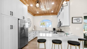 Una cocina moderna con armarios blancos, un refrigerador de acero inoxidable, una isla grande con taburetes de bar y un techo de madera.