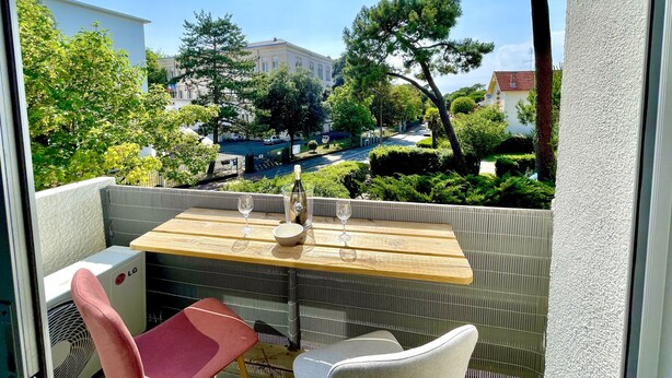 Ein Balkon mit Holztisch, zwei Stühlen und einer Klimaanlage.