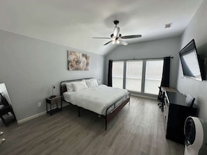 Ein Schlafzimmer mit Bett, Schreibtisch, Stuhl, Deckenventilator und großen Fenstern.