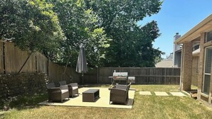 A backyard with a patio area, a grill, and a wooden fence.