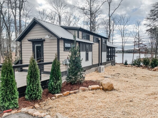 Une cabane dotée d’une terrasse, entourée d’arbres et bordée par un lac.