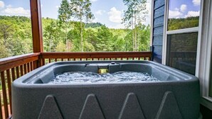 Een hottub op een houten terras met uitzicht op een bos.