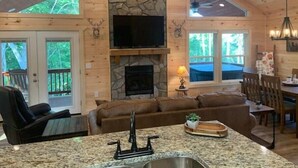 Een gezellig chaletinterieur met een stenen open haard, een televisie erboven en een eethoek met een tafel en stoelen.