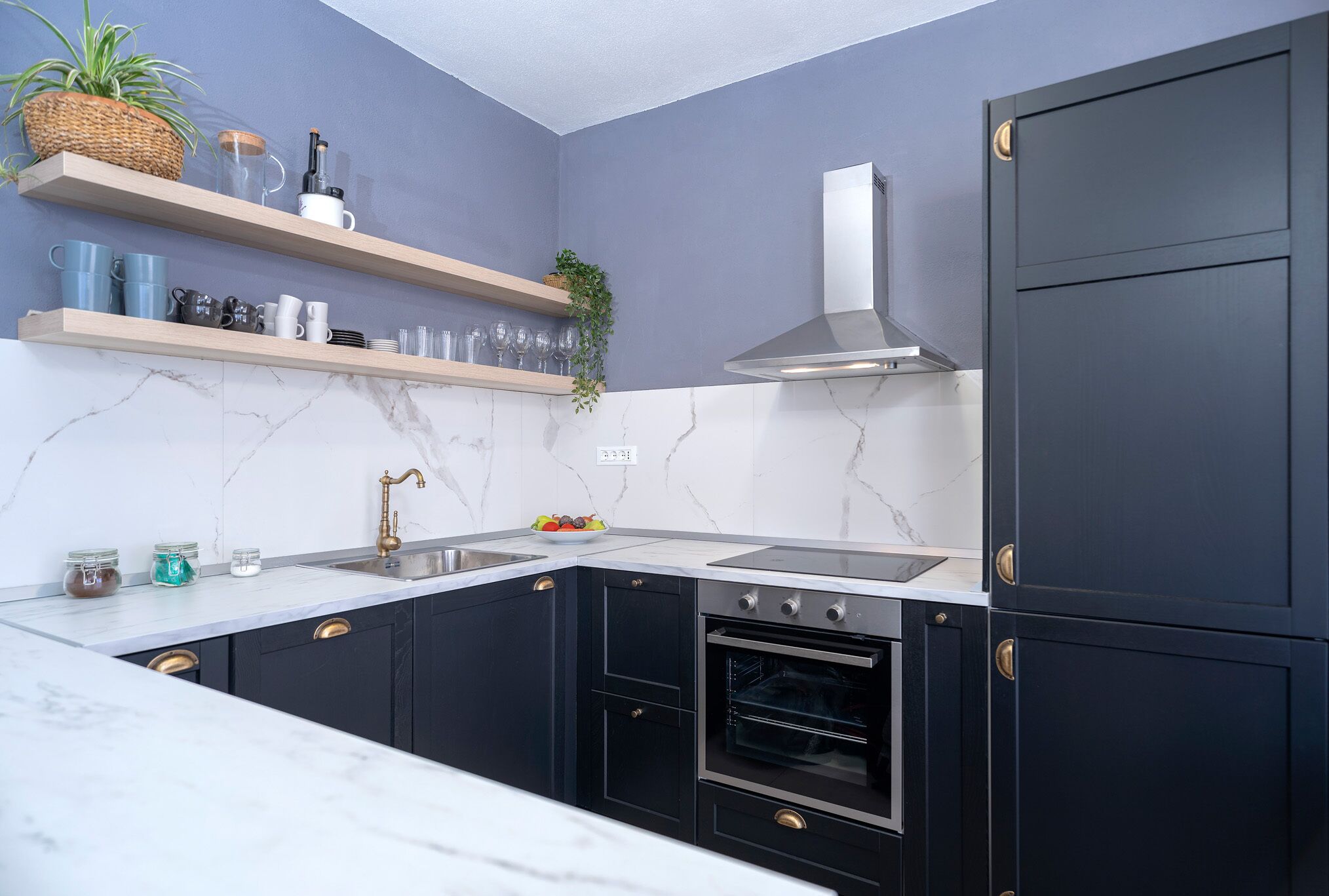 Une cuisine avec des meubles de couleur sombre, une hotte de cuisinière en acier inoxydable et un pare-feu en marbre.