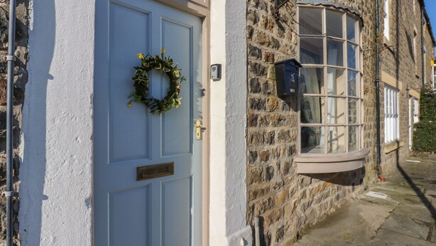 Ein traditionelles Steinhaus mit blauer Tür, einem Fenster mit weißem Rahmen und einem kleinen Blumenkasten.