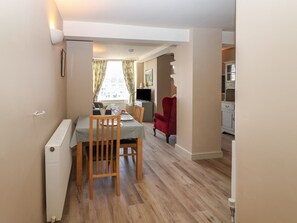 A dining area with a table set for two, a red armchair, and a view of a kitchen and living area. - 8 Market Place (Ripon)