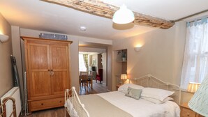Ein Schlafzimmer mit einem Holzschrank, einem Bett mit weißer Bettwäsche, einem Holzboden und einer Decke mit sichtbaren Holzbalken.