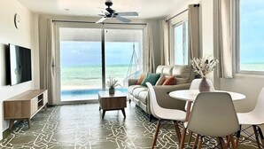 A modern living room with a large sliding glass door leading to a balcony with a view of the ocean. - Beachfront 1 Bedroom/Pool/Kitchen/Breakfast/550SF (San Pedro)
