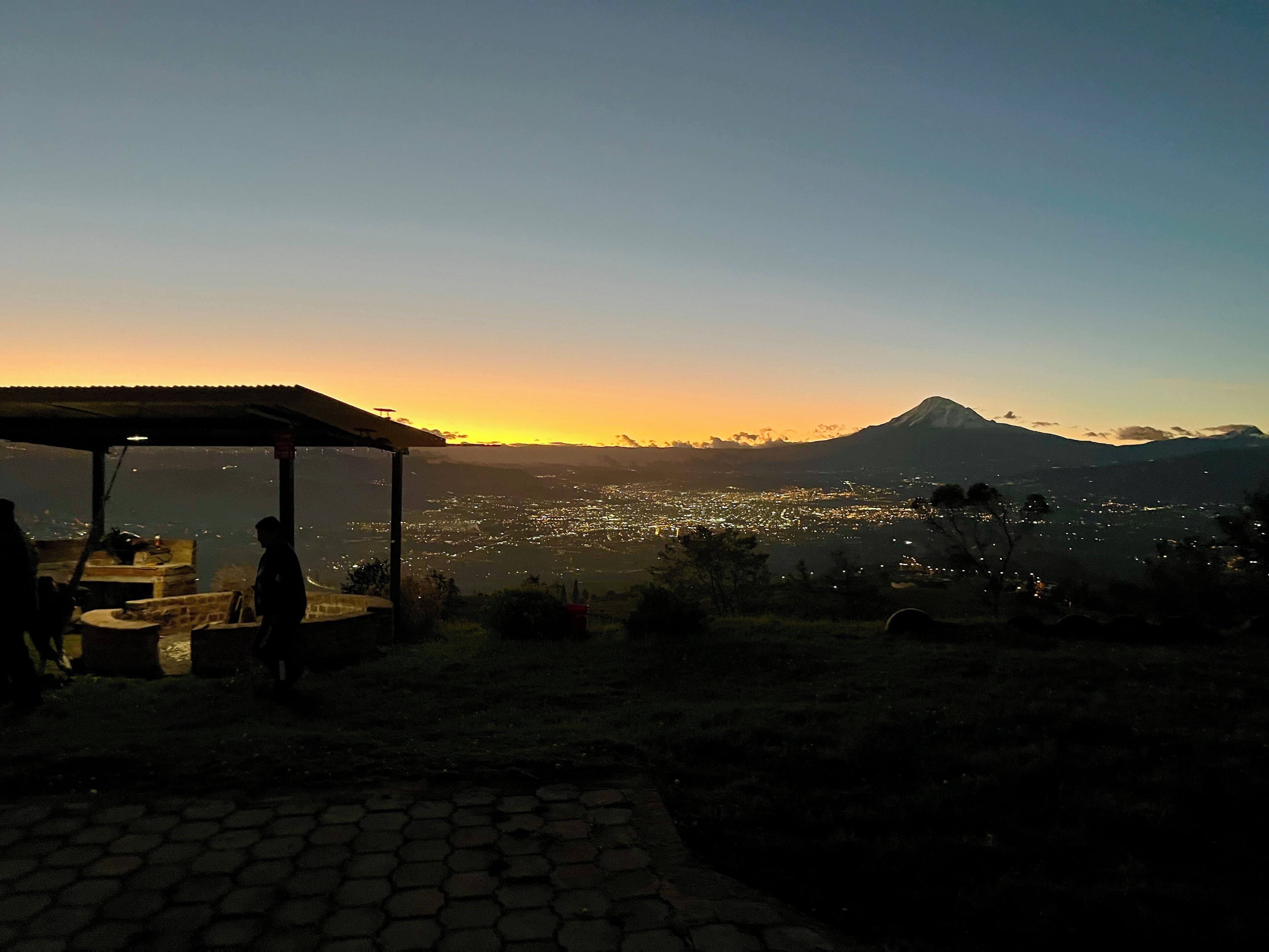 Une vue sur le coucher de soleil depuis une terrasse, avec une montagne en arrière-plan.
