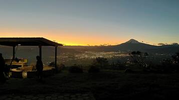 Une vue sur le coucher de soleil depuis une terrasse, avec une montagne en arrière-plan.