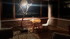 A cozy room with a brick wall, large windows, a wooden table, and a white chair. - Casa Vacacional con Vista al Chimborazo en Chambo (Chambo)
