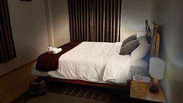 A neatly made bed with a white duvet and brown throw, a bedside table with a lamp, and a small rug on the floor.
