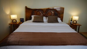 A neatly made bed with a brown bedspread and two pillows, flanked by wooden nightstands with lamps and a wine bottle. - Casa Vacacional con Vista al Chimborazo en Chambo (Chambo)