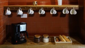 A kitchen area with a brick oven, a coffee machine, hanging mugs, a vase with dried plants, and a tray of bread. - Casa Vacacional con Vista al Chimborazo en Chambo (Chambo)