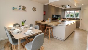 Une cuisine moderne dotée d’un îlot central, d’un coin repas avec une table pour quatre personnes et d’une grande fenêtre laissant entrer la lumière naturelle.