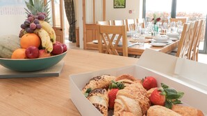 Un coin repas avec une table mise pour le repas, un saladier de fruits et une boîte de pâtisseries.