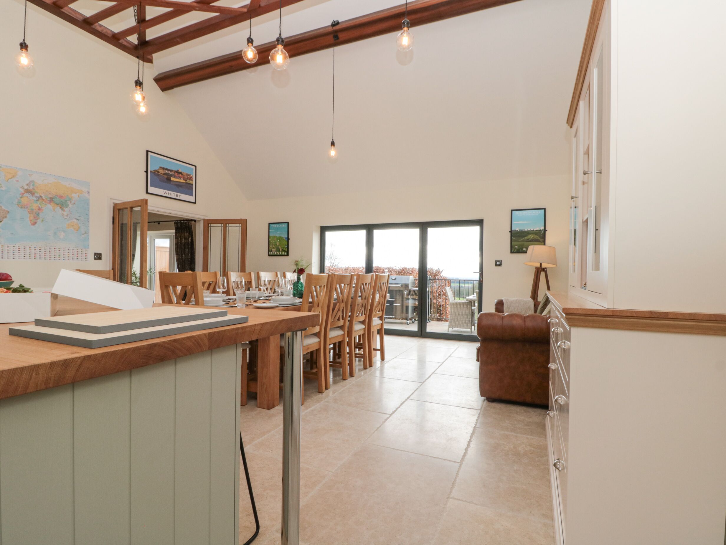 A spacious kitchen with a dining area, wooden ceiling beams, and a view through a glass door to the outside.