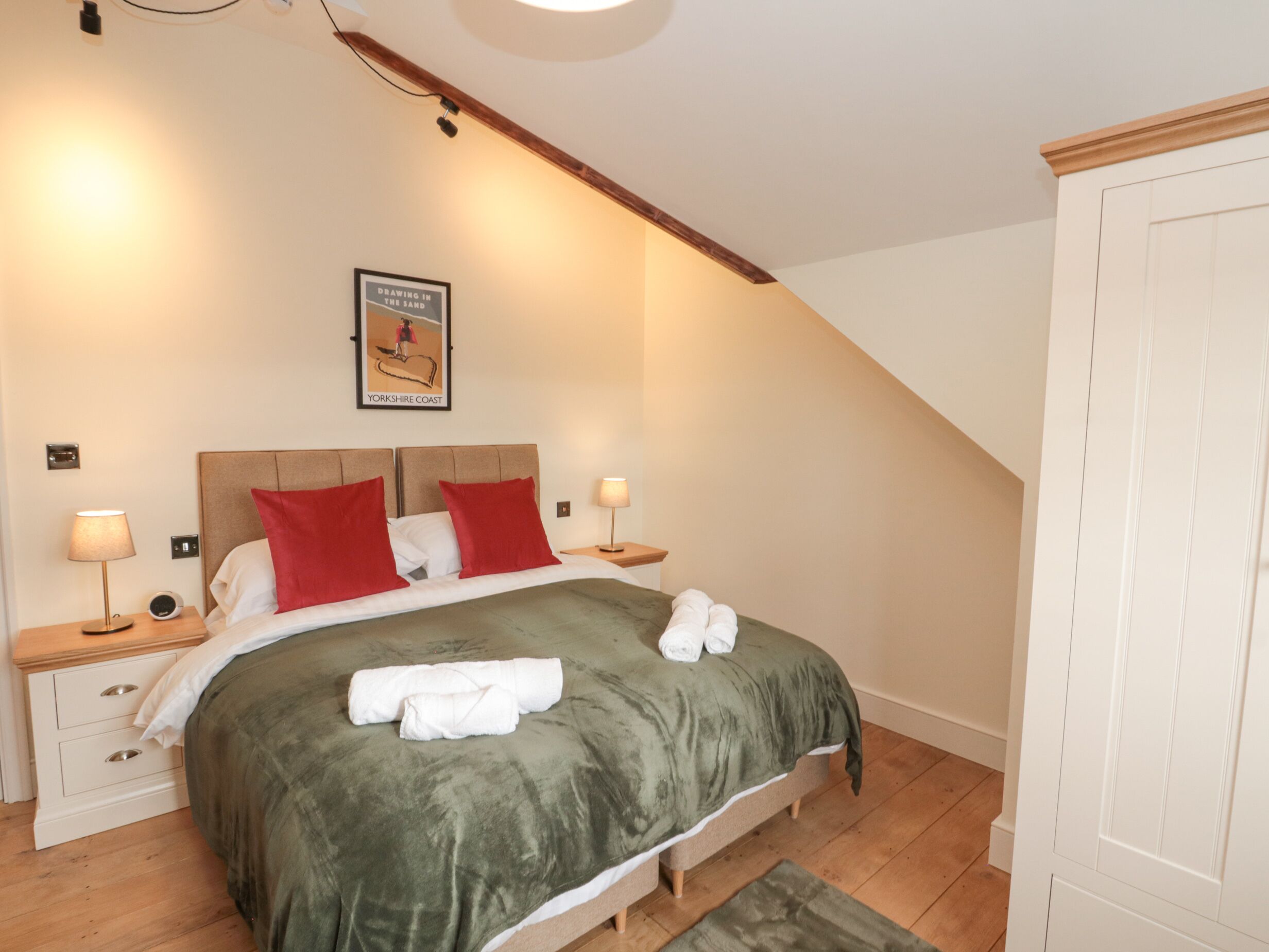 A bedroom with a bed, two nightstands, a framed picture, and a wooden ceiling beam.