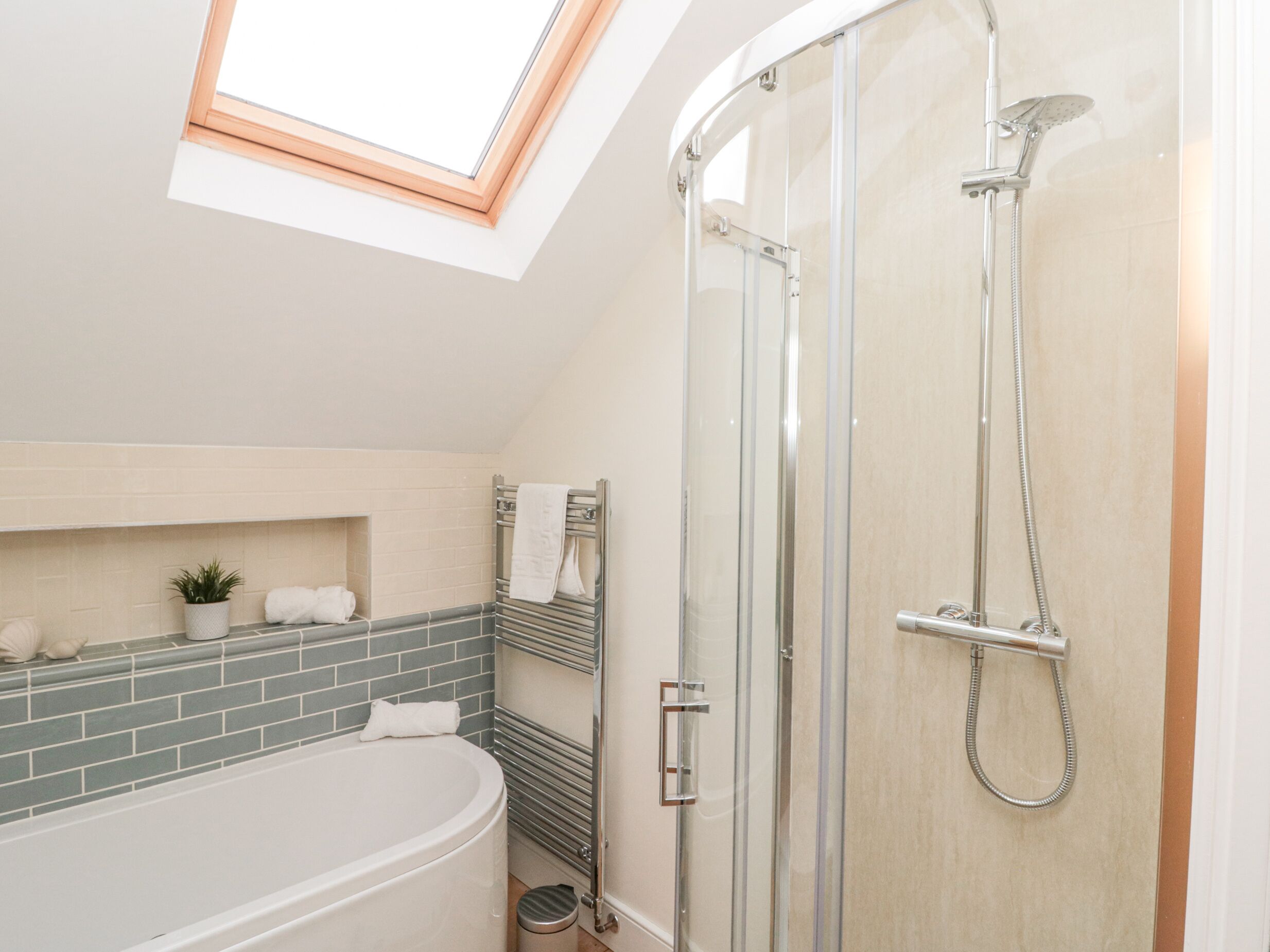 A modern bathroom with a skylight, a freestanding bathtub, a glass-enclosed shower, and a tiled backsplash.