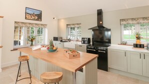 Une cuisine spacieuse dotée d’un grand îlot central, de tabourets de bar en bois, d’une hotte noire et offrant une vue sur la verdure environnante.