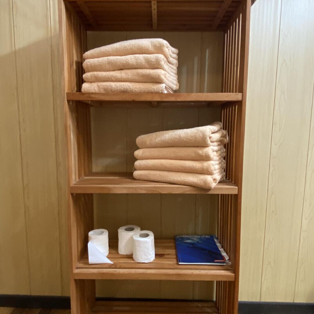 A wooden shelf unit with folded towels and toilet paper.