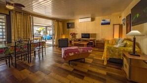 A cozy room with a wooden floor, a bed, a sofa, a TV, and a dining table with chairs.