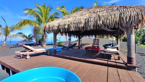 A wooden deck with lounge chairs, a thatched-roof structure, and a pool.