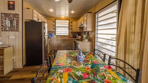 A compact kitchen with wooden cabinets, a black refrigerator, a dining table with a floral tablecloth, and a ceiling fan.