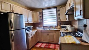 Una cocina compacta con armarios de madera, un refrigerador de acero inoxidable, un microondas, un fregadero y una estufa.