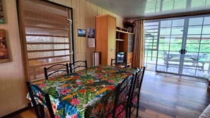 Un comedor con una mesa cubierta con mantel floral, sillas de madera y un ventanal corredero que da a un patio exterior.