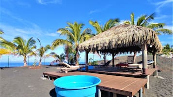 A beach with a thatched-roof hut, wooden benches, and a blue pool.
